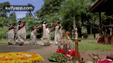 a group of women are dancing in front of a floral display .