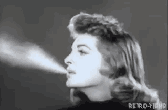 a black and white photo of a woman blowing smoke out of her mouth .