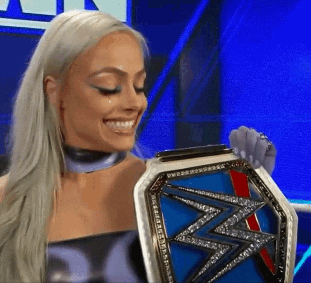 a woman is holding a wrestling championship belt in her hands and smiling .