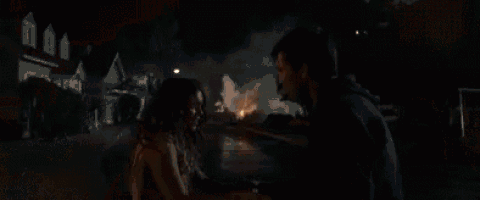 a man and a woman are holding hands in front of a fire explosion .