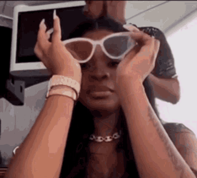 a woman wearing sunglasses is making a funny face while holding her hands to her face .