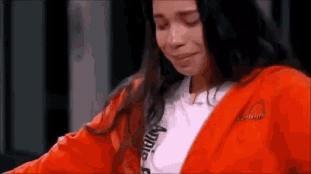 a woman in an orange jumpsuit is crying while wearing a white t-shirt .