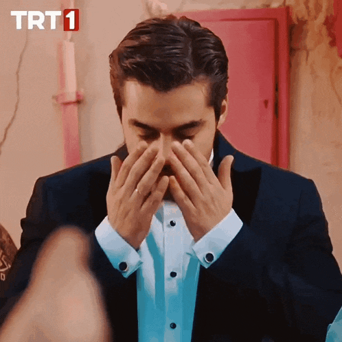 a man in a suit is covering his face in front of a pink door that says trt1 on it