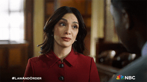 a woman in a red coat is talking to a man in a suit with a nbc logo in the corner