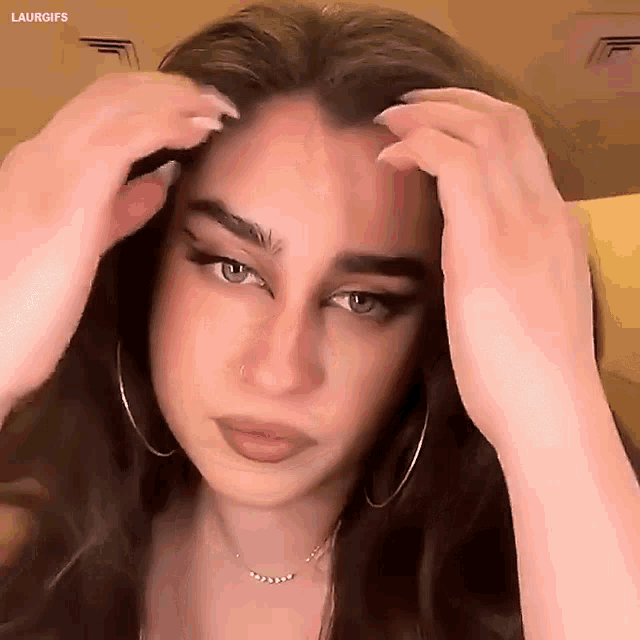 a woman wearing hoop earrings and a necklace is holding her hair .