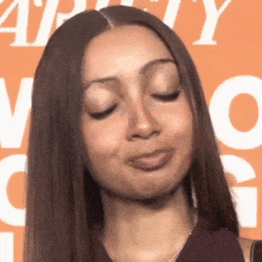 a woman making a funny face with her eyes closed in front of an orange sign that says " ability "