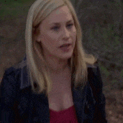 a woman in a black jacket and a red top is standing in the woods .