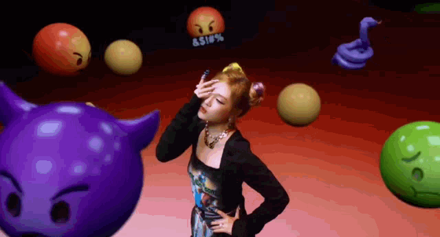 a woman is standing in front of a bunch of balls with emojis on them .