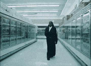 a man in a long black coat walks through an empty supermarket aisle