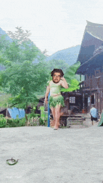 a man in a green skirt is walking in front of a wooden building with mountains in the background