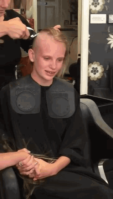 a woman is getting her hair cut in a salon with a black cape that says ' sally ' on it
