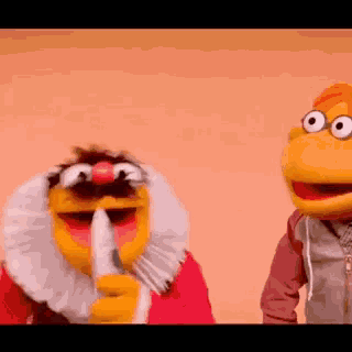 a couple of muppets are standing next to each other and one is holding a finger to his mouth .