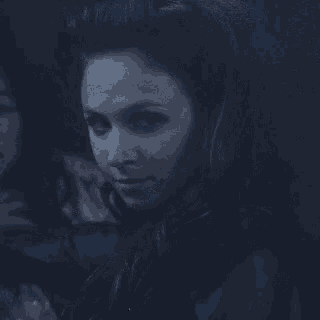a close up of a woman 's face in a dark room with a ponytail .