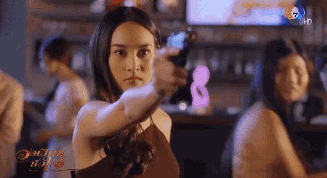 a woman is pointing a gun at the camera while sitting at a bar .