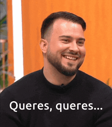 a man with a beard is smiling and wearing a black shirt that says queres