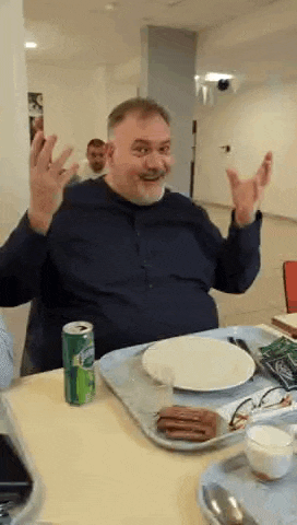 a man with a beard is sitting at a table with a plate of food and a can of sprite .