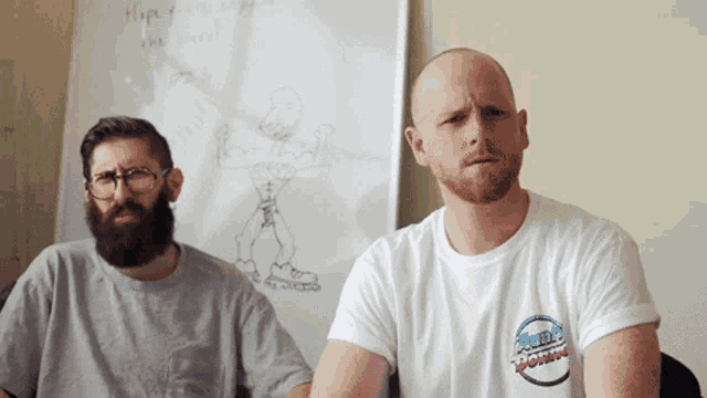 two men are sitting in front of a white board with a drawing on it