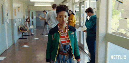 a girl in a green jacket is standing in a hallway in a school .