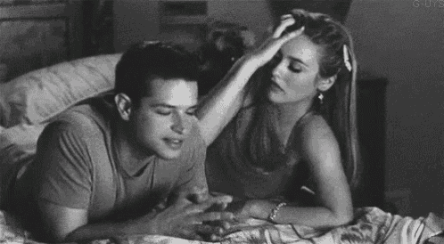 a man and a woman are laying on a bed . the woman is touching the man 's head .