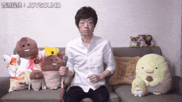 a man sitting on a couch holding a microphone with joysound written in the corner