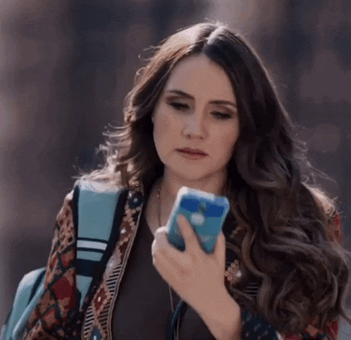 a woman is looking at her cell phone while wearing a backpack .