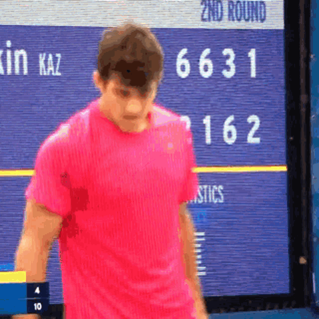 a man in a pink shirt stands in front of a screen that says 2nd round on it