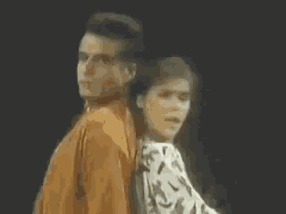 a man and a woman are standing back to back and looking at the camera .