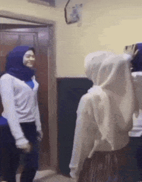 a group of women are standing next to each other in a room . one of the women is wearing a hijab .