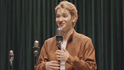 a man in a brown jacket stands in front of two microphones