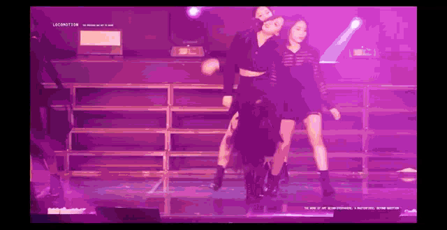 a group of women are dancing on a stage in a purple light .