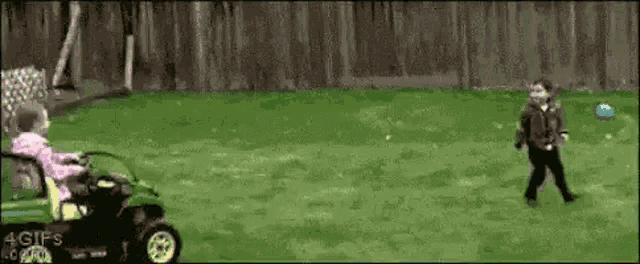 a girl is riding a lawn mower in a backyard while a boy runs towards her .