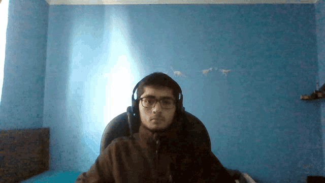 a man wearing headphones and glasses is sitting in a chair in front of a blue wall