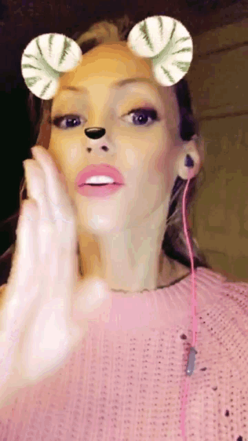 a woman wearing a pink sweater and headphones has a fake nose and ears on her face