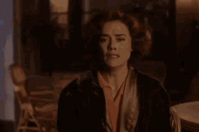 a woman is standing in a dark room with a scarf around her neck and looking at the camera .