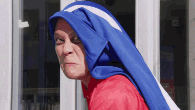 a woman with a blue and white scarf around her head looks at the camera
