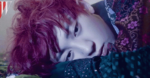 a person with red hair is laying on a bed with a floral shirt on .