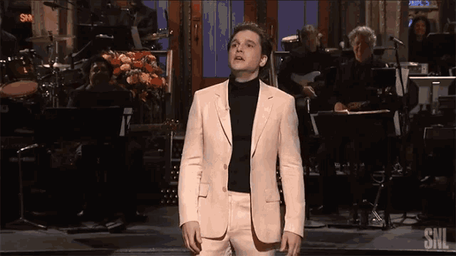 a man in a suit stands in front of a snl band