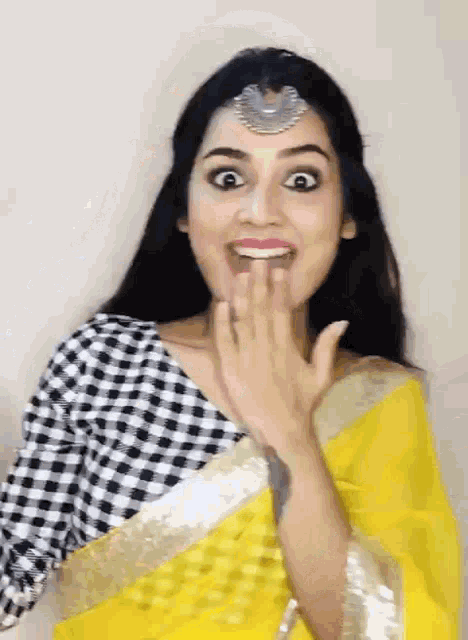 a woman in a yellow saree and black and white checkered blouse is making a funny face .