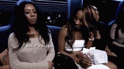 two women are sitting next to each other on a couch . one of the women is holding a bag of money .