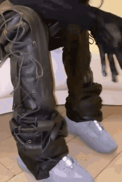 a person wearing black leather pants and a pair of white sneakers