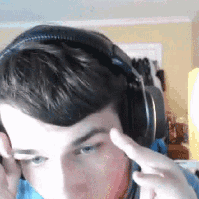a young man wearing headphones is pointing at his forehead