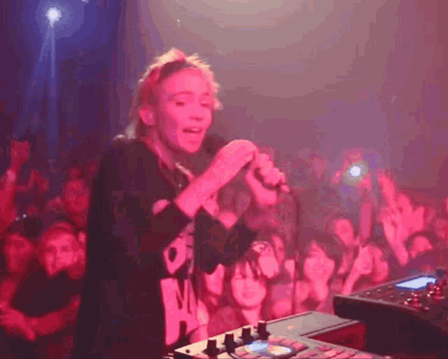 a woman singing into a microphone in front of a crowd wearing a black shirt that says ' o ' on it