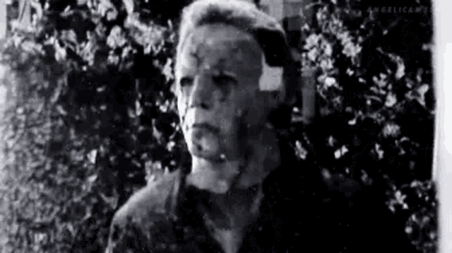 a black and white photo of a man with a bandage on his head standing in front of a tree .