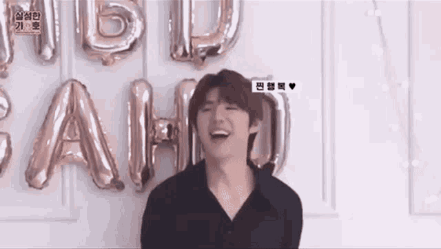 a man in a black shirt is laughing in front of balloons that spell out the word happy birthday .