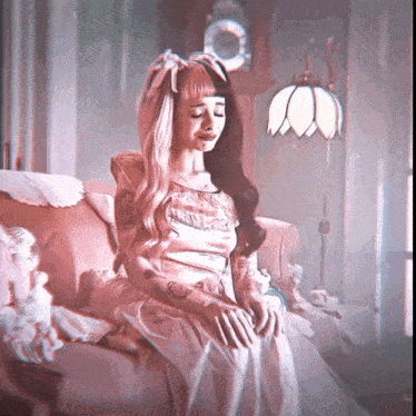 a woman is sitting on a couch with a lamp and a clock in the background