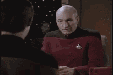 a bald man in a red shirt is covering his face with his hands