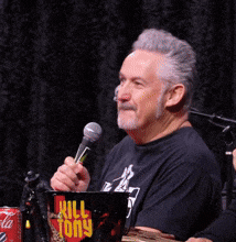 a man is holding a microphone in front of a mug that says kill tony