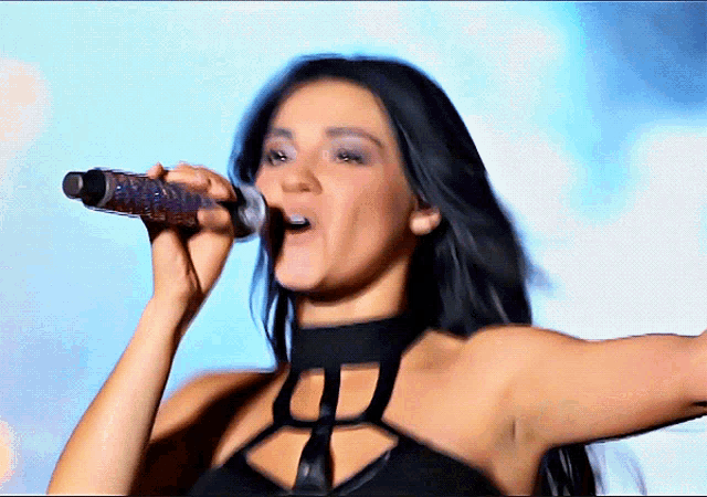 a woman singing into a microphone with a choker on her neck