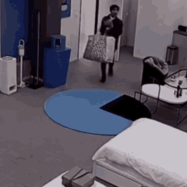 a man is carrying a bag in a room with a bed and chairs .