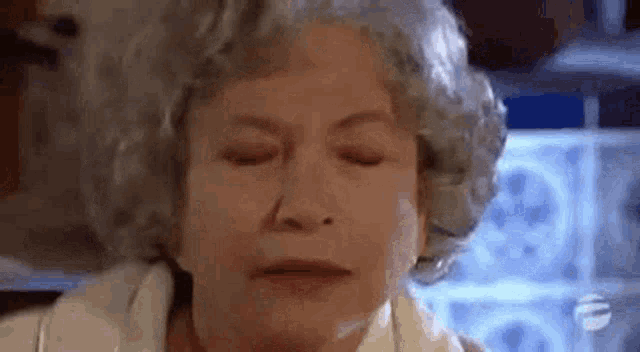 an elderly woman with gray hair is making a funny face with her eyes closed .